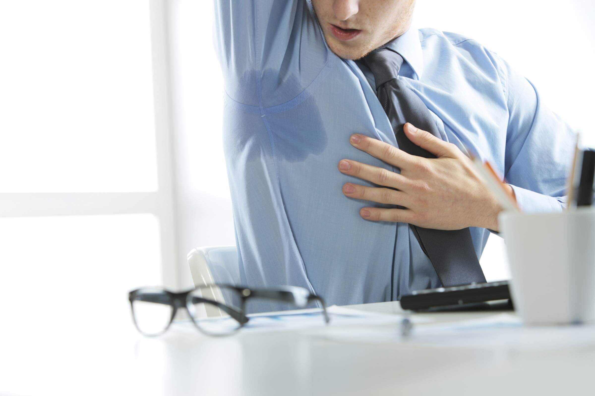 Man at desk checking out a sweat mark on his shirt.