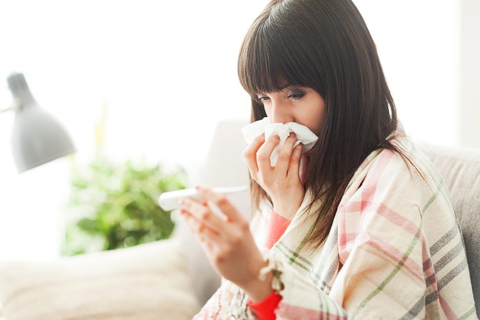 woman holding a tissue to her nose while she reads a thermometer