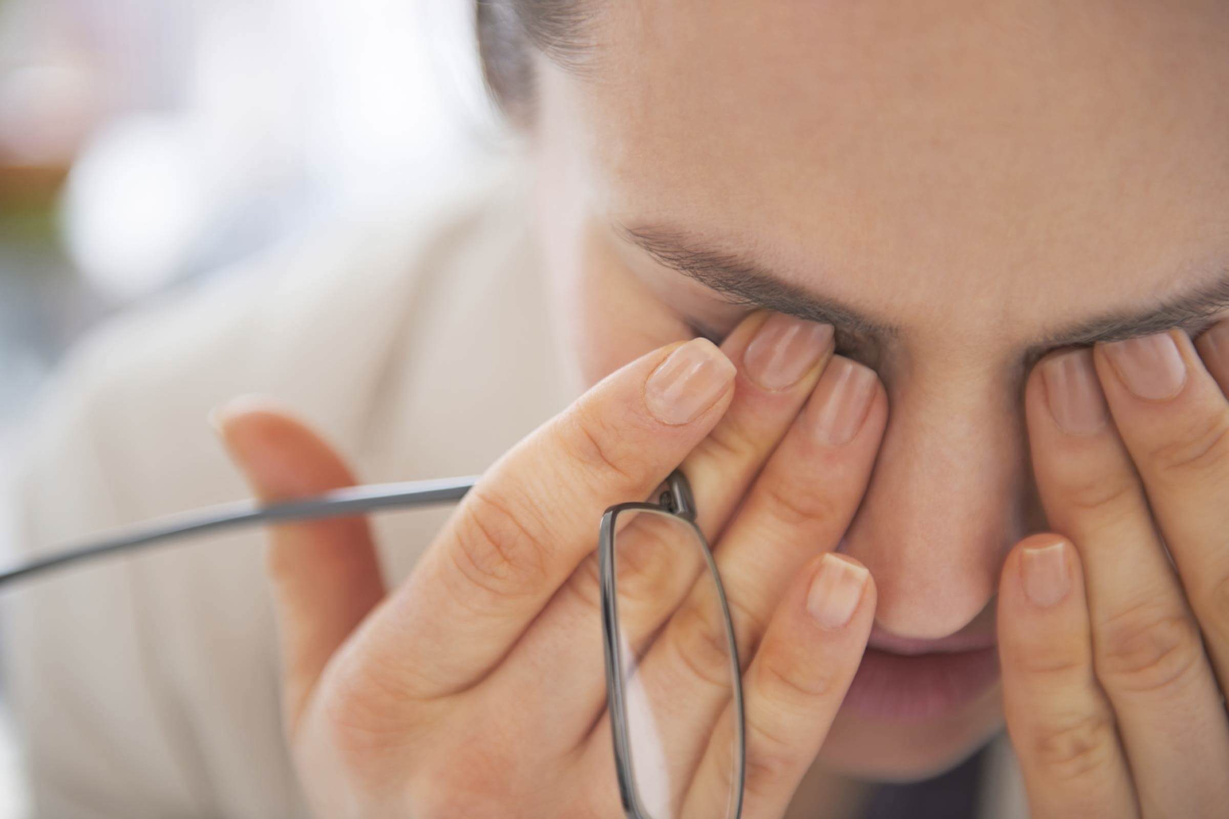 Woman with tilted head presses her fingers against her tired eyes.