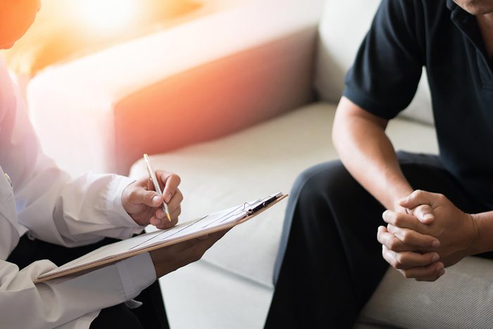 Person sitting on a couch in a doctor's office as a doctor takes notes.