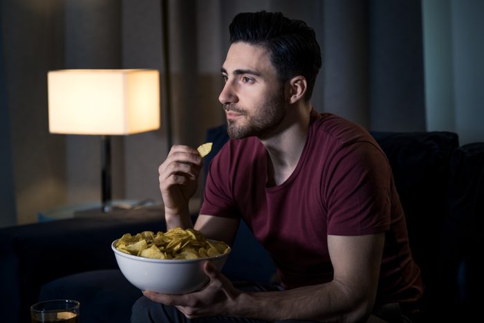 man eating chips while watching a movie at home