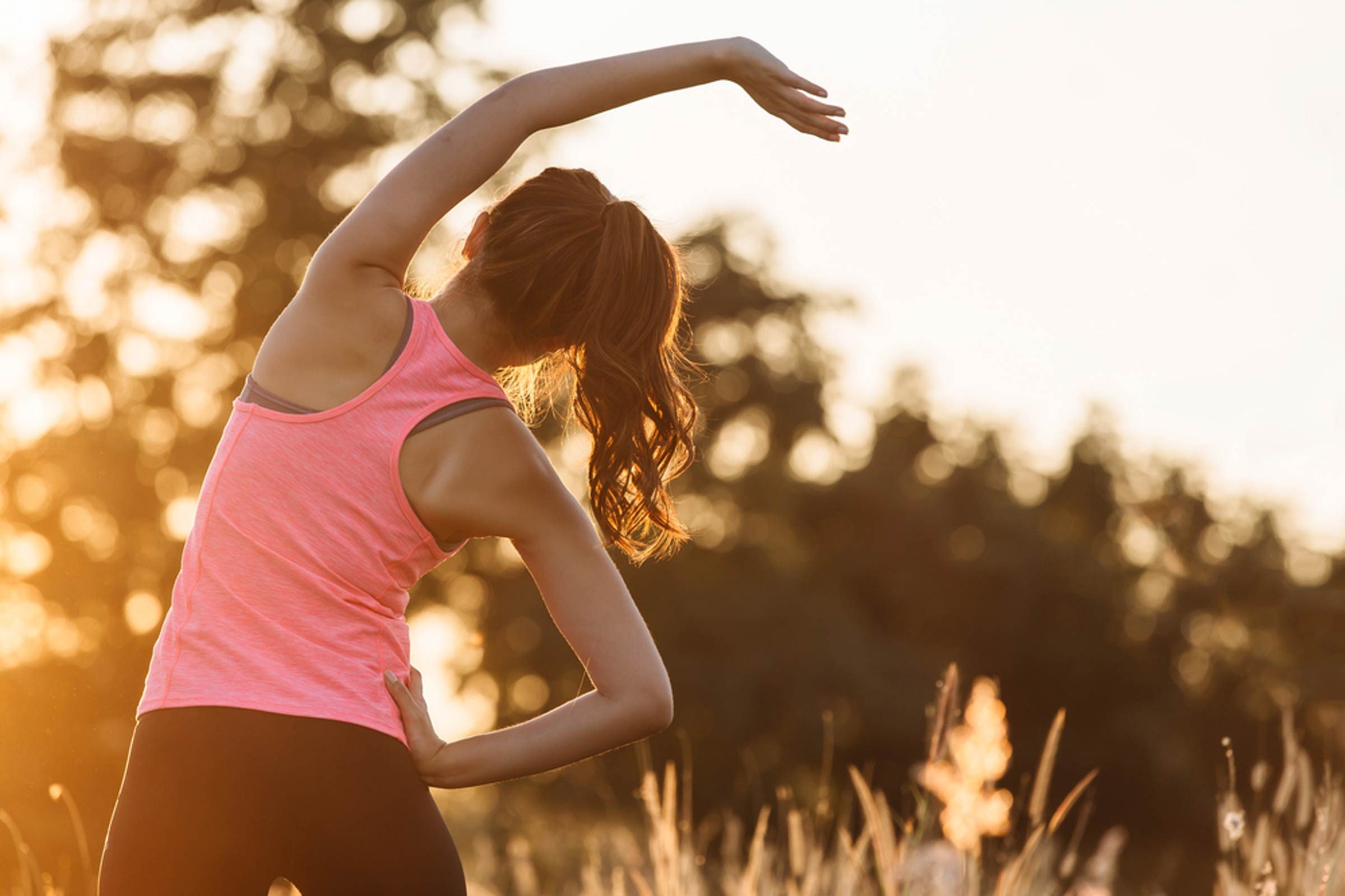 Woman in a pink tank top stretching outdoors.