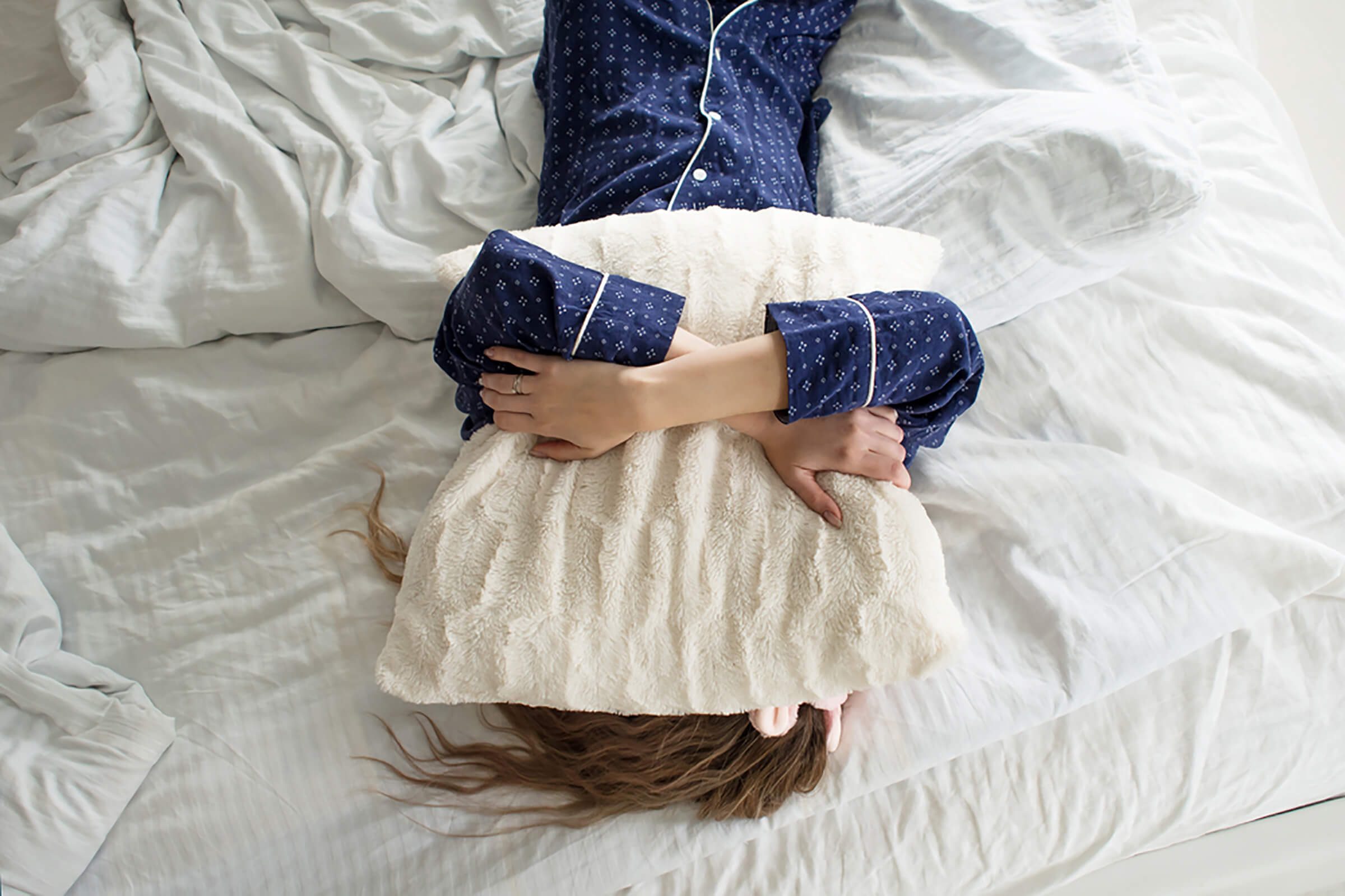 woman with pillow over her face in bed