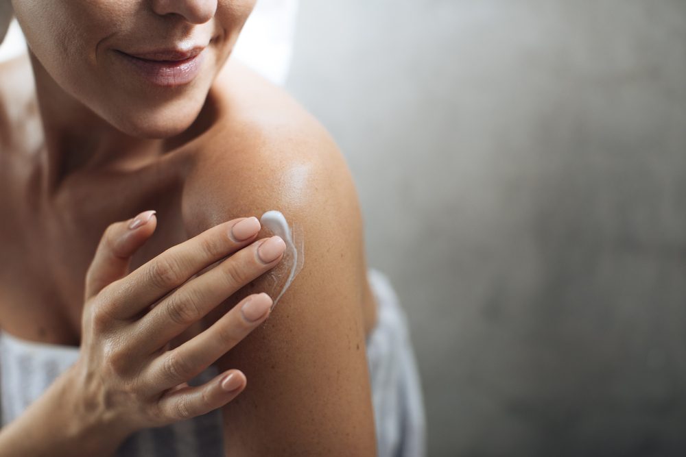 woman putting moisturizer on her shoulder