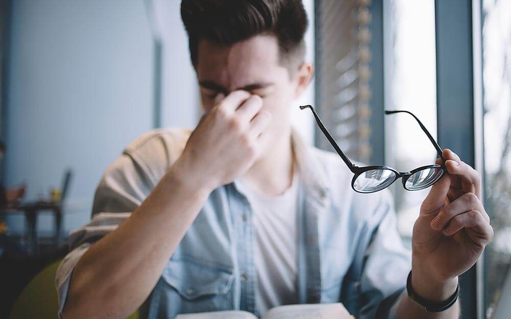 man reading book, glasses off, blurry vision, headache