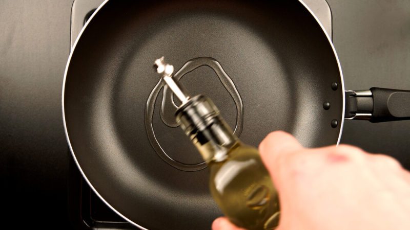 TOP VIEW: Human hands pouring olive oil on the frying pan