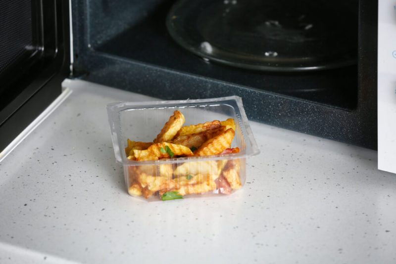 Plastic container with lunch near microwave oven on table in kitchen. Cooking for one concept