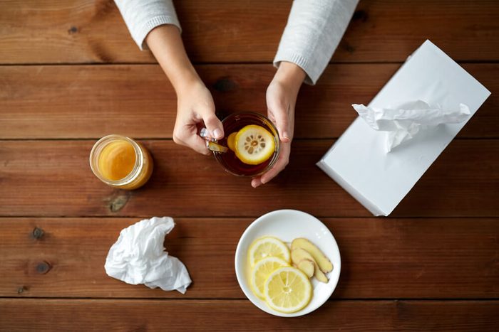 health, traditional medicine and ethnoscience concept - ill woman drinking tea with lemon, honey and ginger and paper wipes box on wooden table