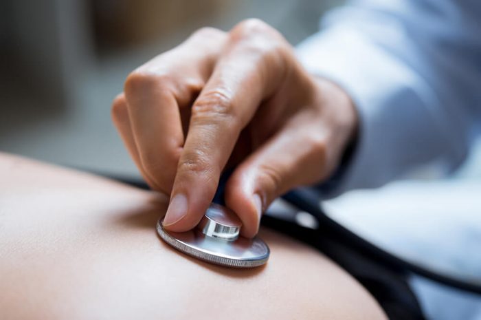 Doctor examining patient with stethoscope. Close up of a doctor hand listening to stethoscope beat while testing patient. Patient visiting doctor for regular check up.