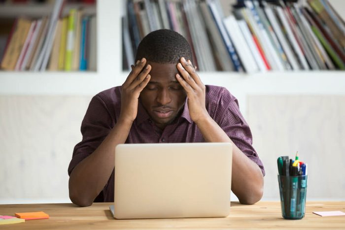 Frowning man looking at computer with head in hands