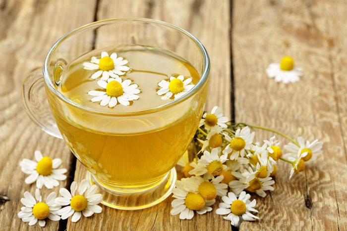 glass mug of chamomile tea topped and surrounded by chamomile flowers