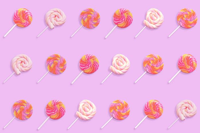 Pattern of colorful lollipop candy with stick isolated on violet background. Flat lay.