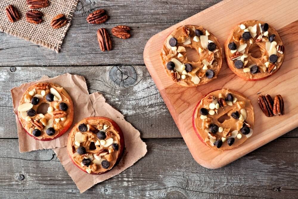 Autumn apple rounds with peanut butter, chocolate chips and nuts, downward view on rustic wood