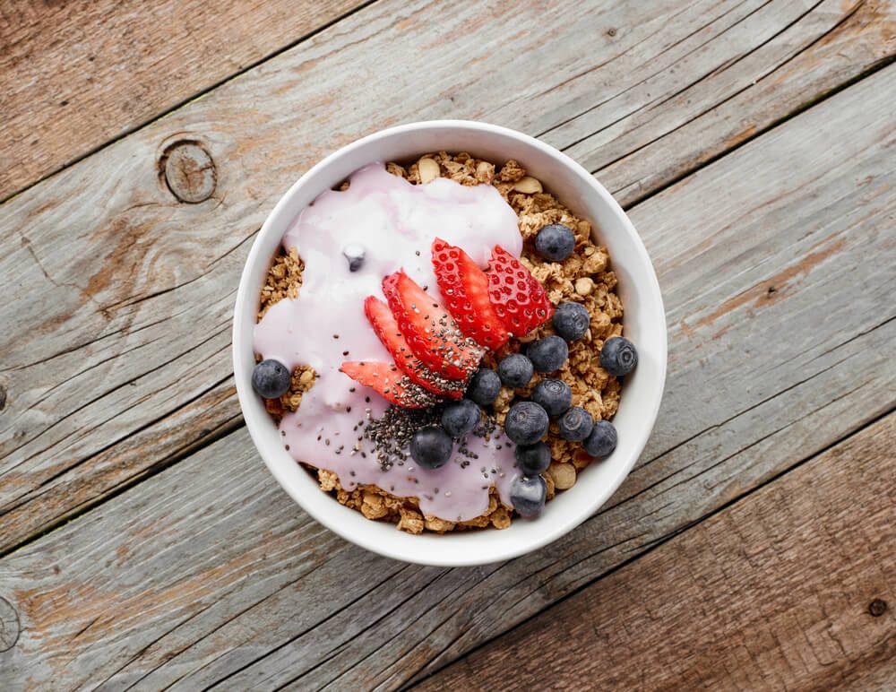 Heart healthy diet; bowl of muesli with yogurt and berries on wooden table, top view