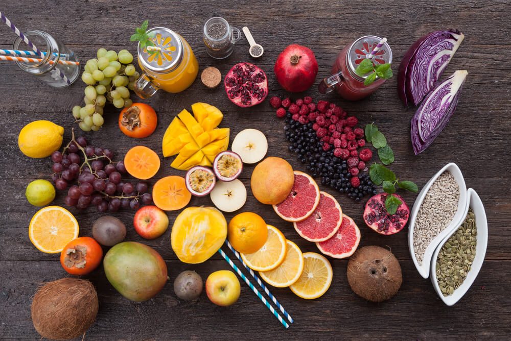 Fruits and frozen berries on dark rustic wooden table. Purple and yellow smoothie bowl formula. Clean eating concept. Various green and red veggies, fruit and superfoods ready to prepare smoothie bowl