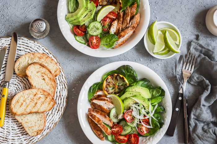 Grilled chicken and fresh vegetable salad on a light background, top view.