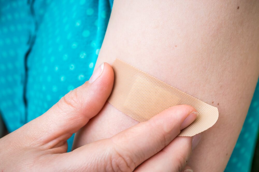 Young woman puts a plaster on her injured arm