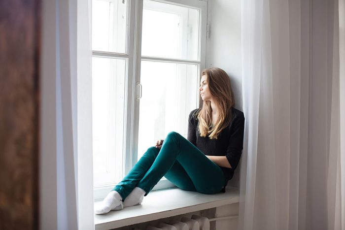 sad woman sitting on window ledge