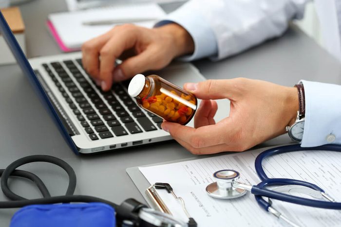 Male medicine doctor hands hold jar of pills and type something on laptop computer keyboard. Panacea and life save, prescribing treatment, legal drug store, take stock, consumption statistics concept
