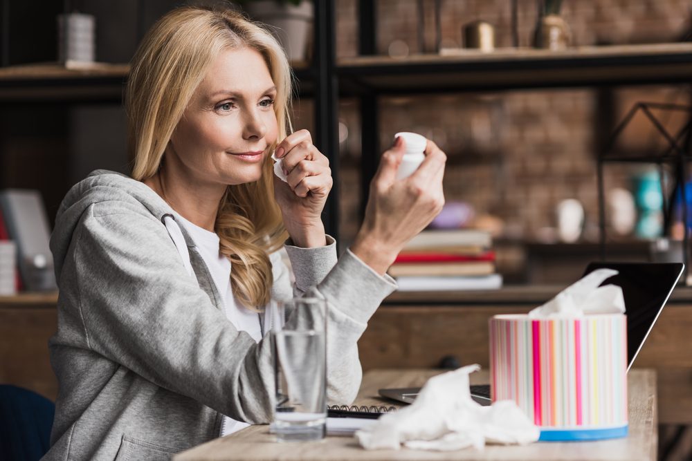 smiling middle aged woman looking at container with medication while sitting at home