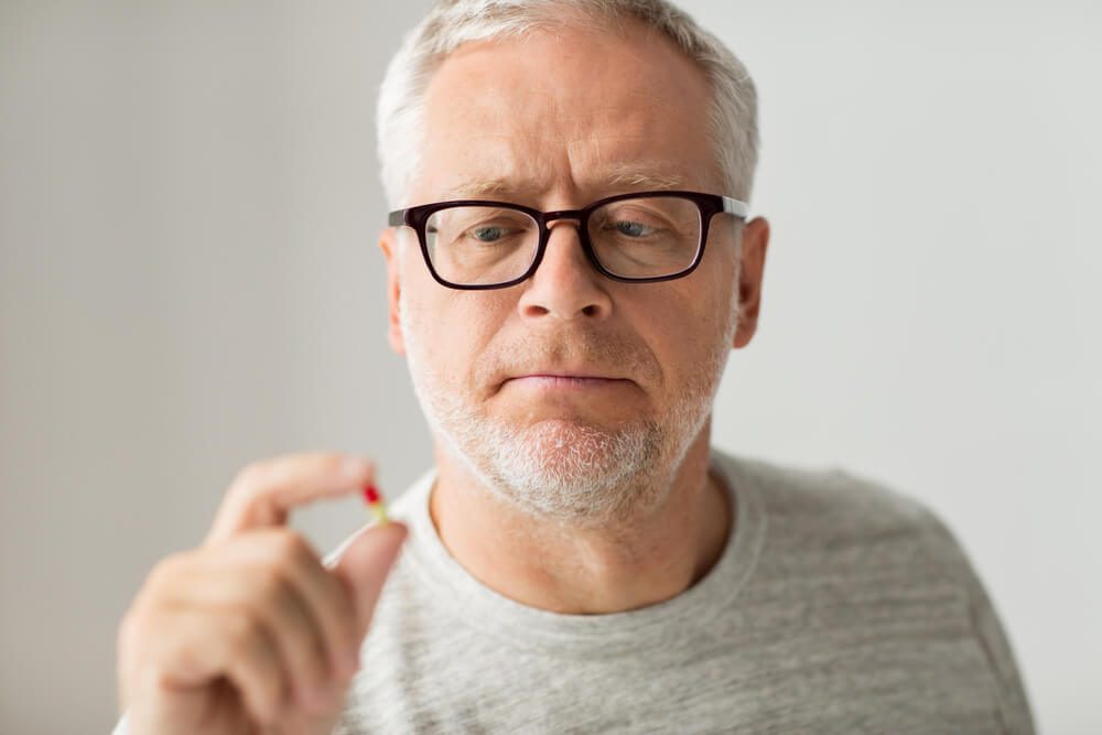 age, medicine, health care and people concept - close up of senior man taking medicine pill at home