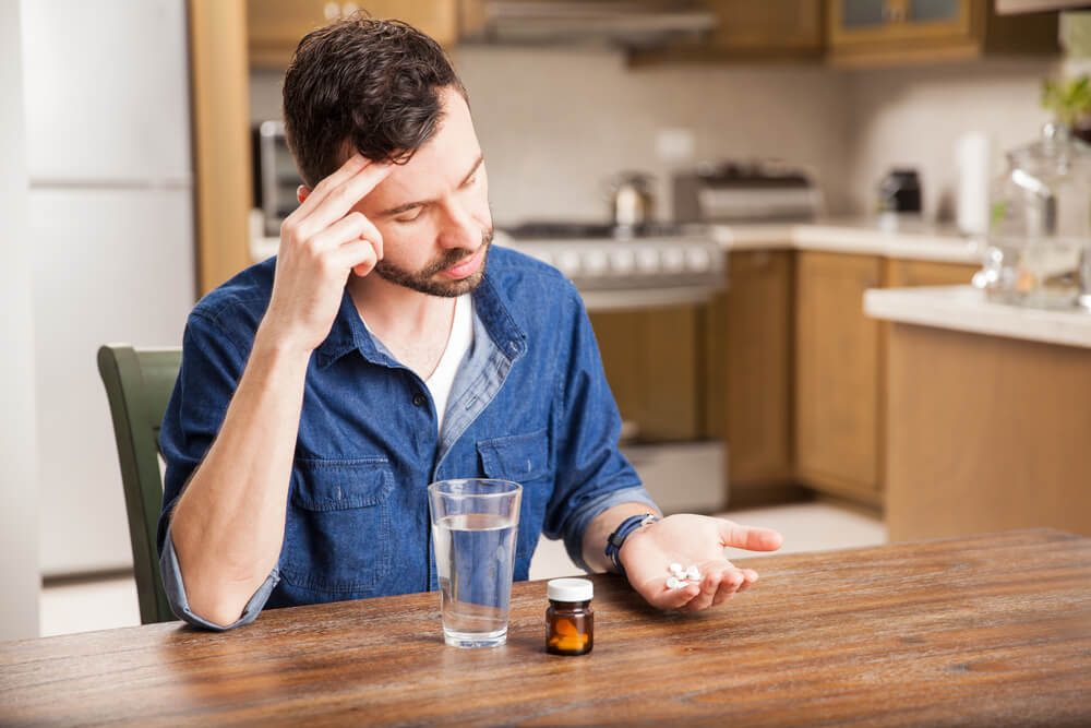 Young hungover man taking some pills to cure a headache at home