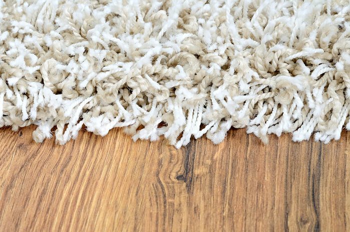 Close-up detail of white shaggy carpet on brown wooden floor