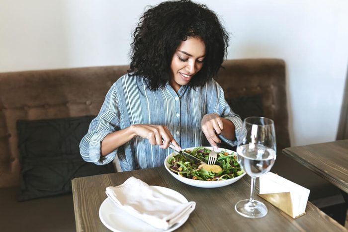 Young womaneating salad in restaurant. Beautiful girl with dark curly hair sitting at cafe and eating salad. Portrait of smiling lady that have lunch in restaurant