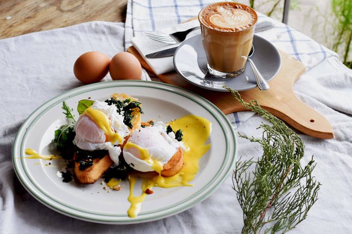 Breakfast Set, Egg benedict in white dish and a great coffee. Latte art. Wood background.