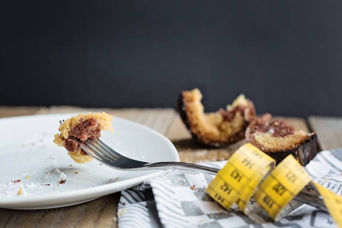 piece of cake impaled on a fork with a measuring tape on a side and broken half-eaten cake at the background