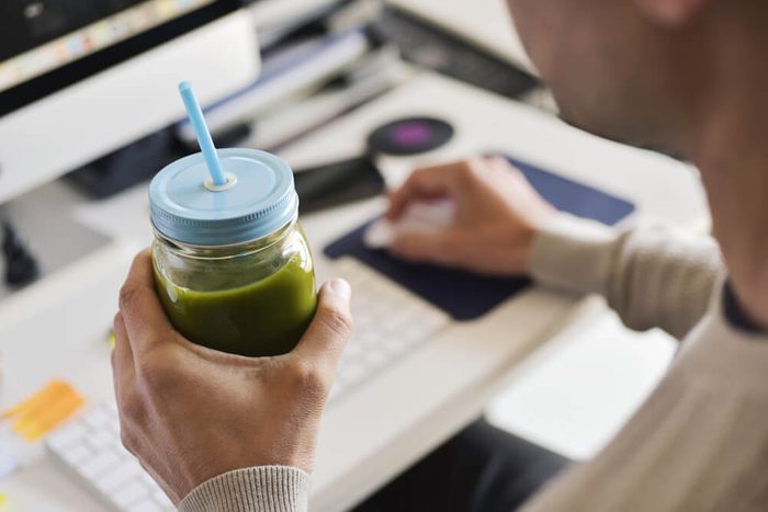 closeup of a young man drinking a green smoothie served in a glass jar at the office