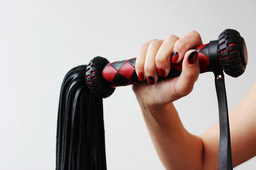 The handle of a red and black lash in a female hand on a white background.