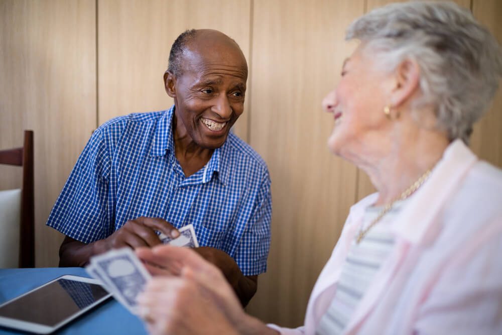 Smiling senior male and female friends playing cards at table in nursing home