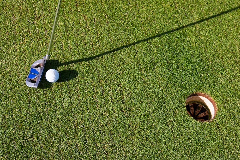 Closeup photo of a short putt. Overhead viewpoint, nobody in the image, with long morning shadows.