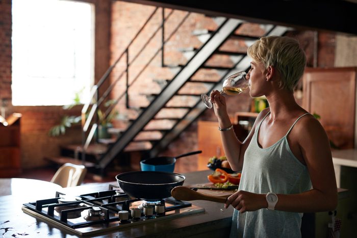 young woman drinking a glass of wine while cooking in the kitchen