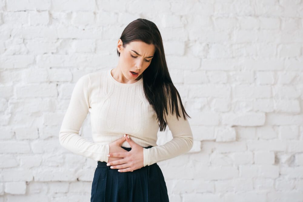 Woman with stomach pain over brick wall.