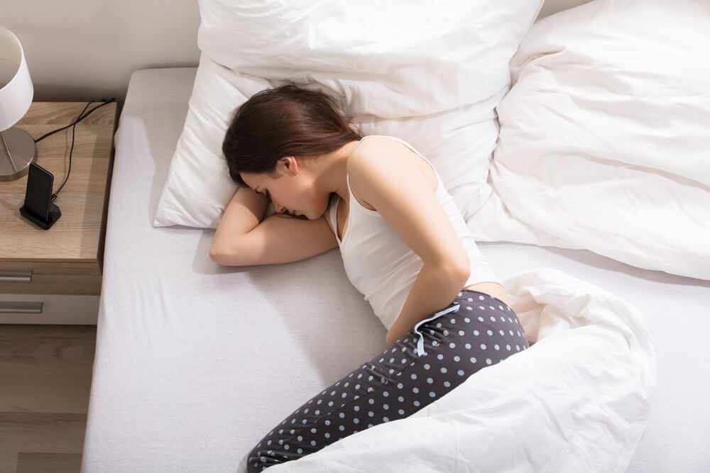 Elevated View Of A Woman Lying On Bed Having Stomach Pain