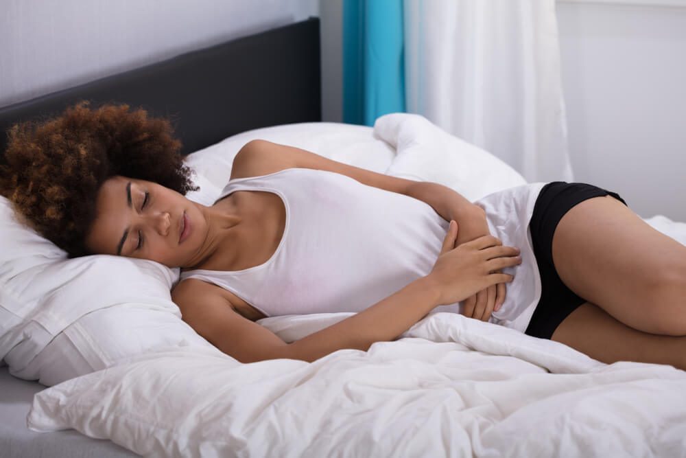 Young Woman Suffering From Stomach Pain Lying On Bed In Bedroom