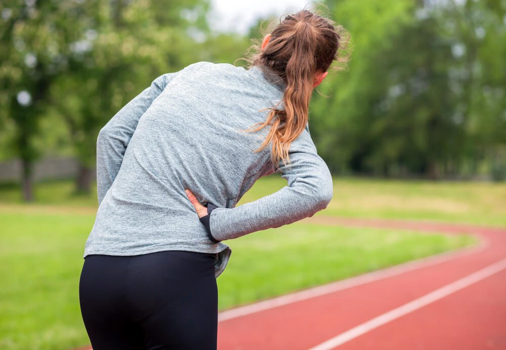 Athletic woman on running track has side cramps during workout