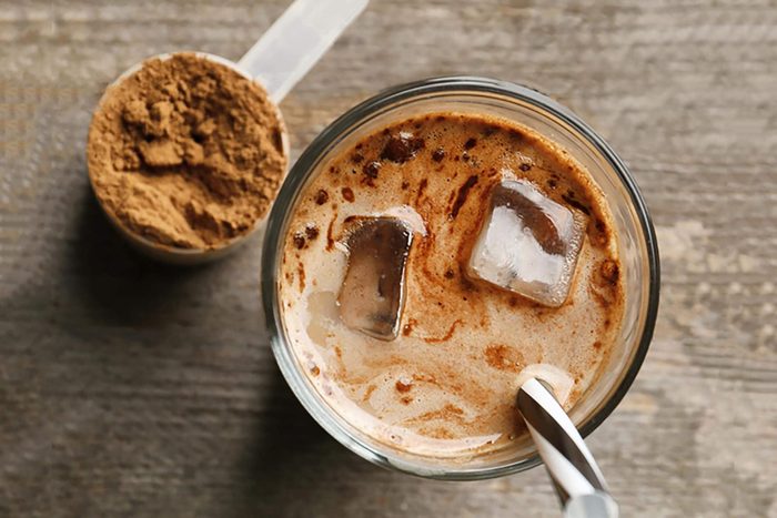 Glass with protein shake and powder in scoop on wooden table