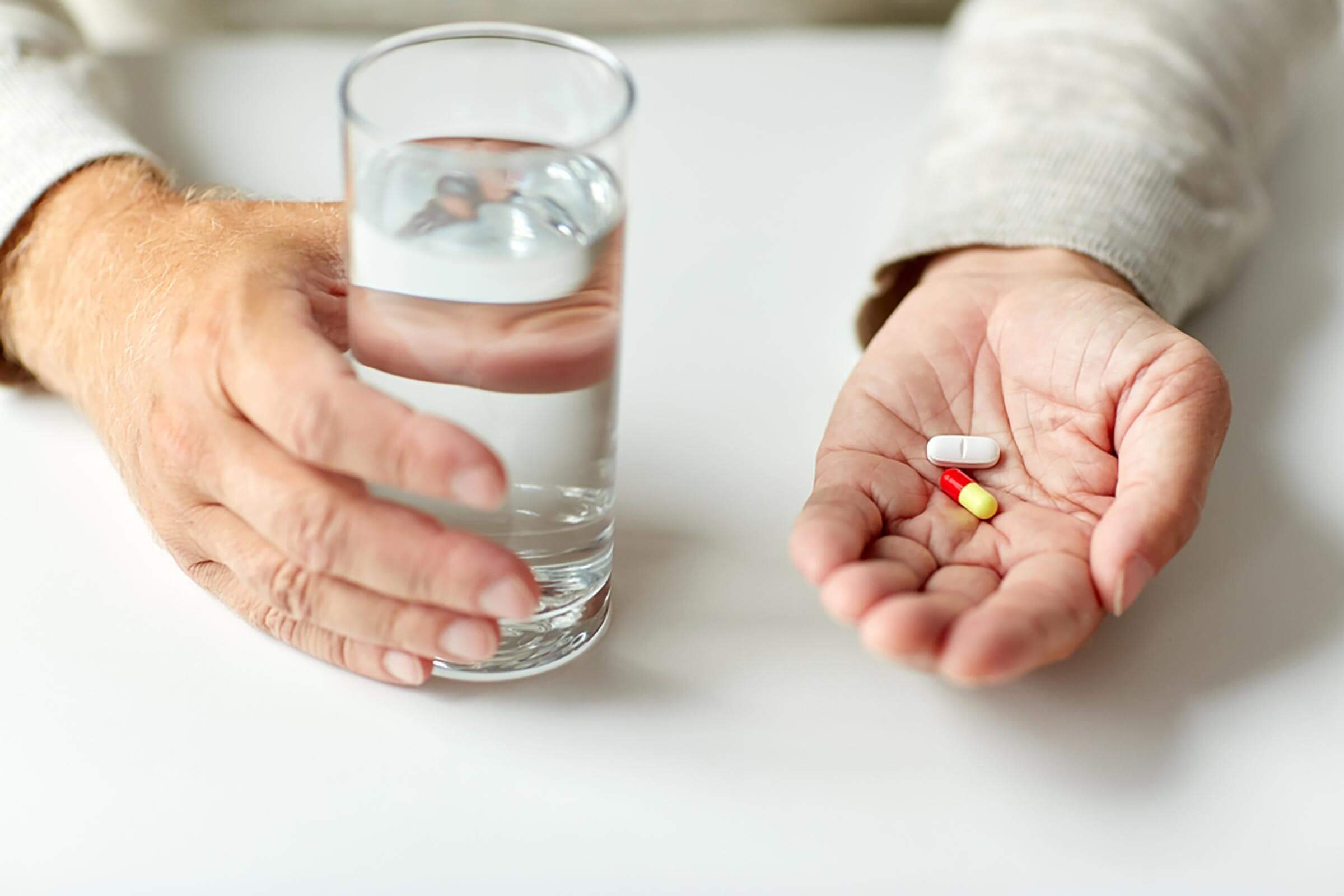 age, medicine, healthcare and people concept - close up of senior man hands with pills and water