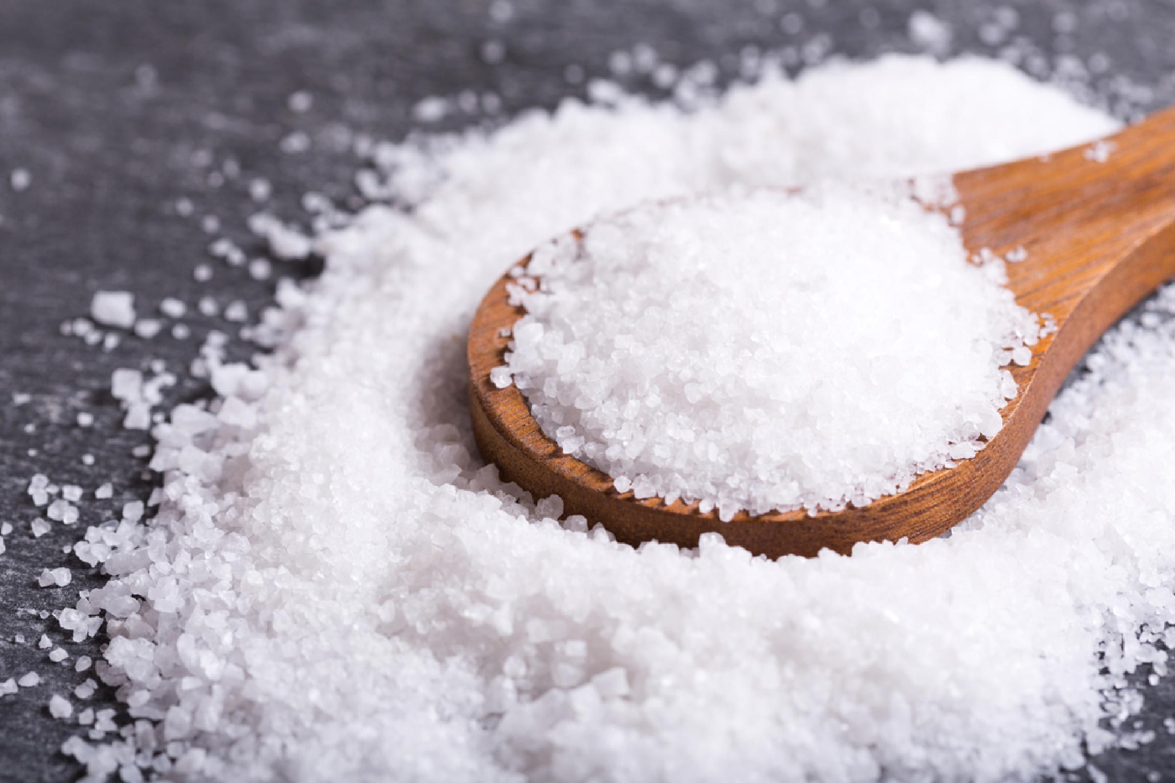 sea salt in a wooden spoon on dark table.