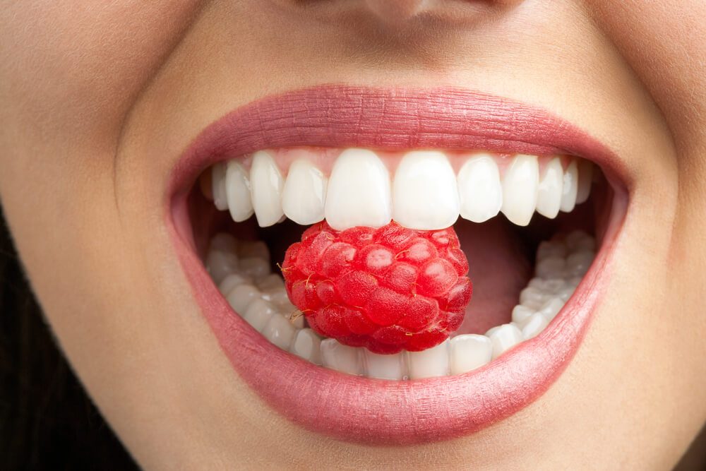 Macro close up of healthy female teeth biting raspberry.