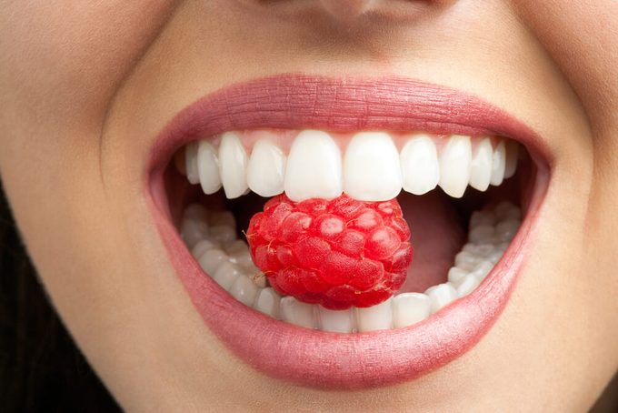Macro close up of healthy female teeth biting raspberry.