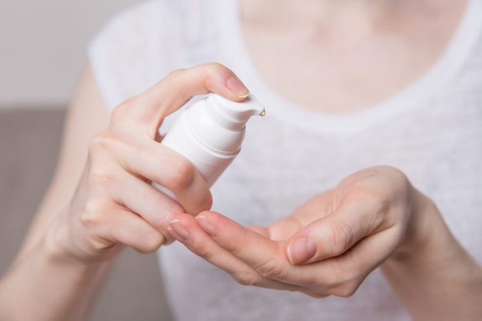 Women's hands using wash hand sanitizer gel pump dispenser.