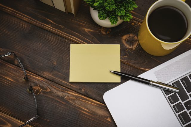 sticky note on desk next to laptop coffee and glasses