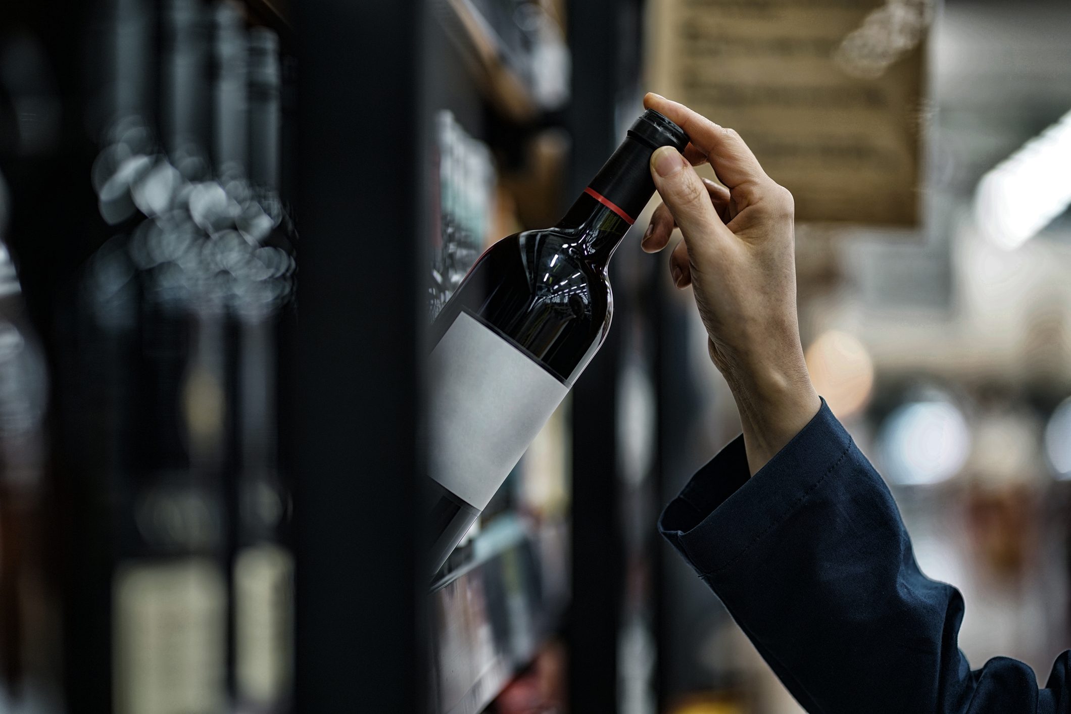 close up of woman's hand grabbing wine off of shelf at store