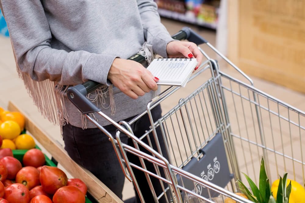 Woman with notebook in grocery store, closeup. Shopping list on paper.