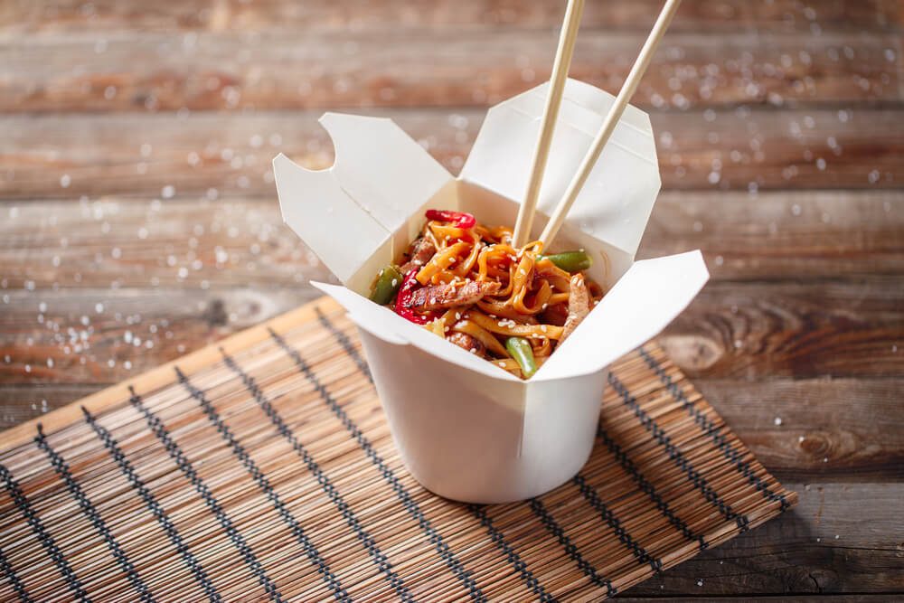 Noodles with pork and vegetables in take-out box on wooden table