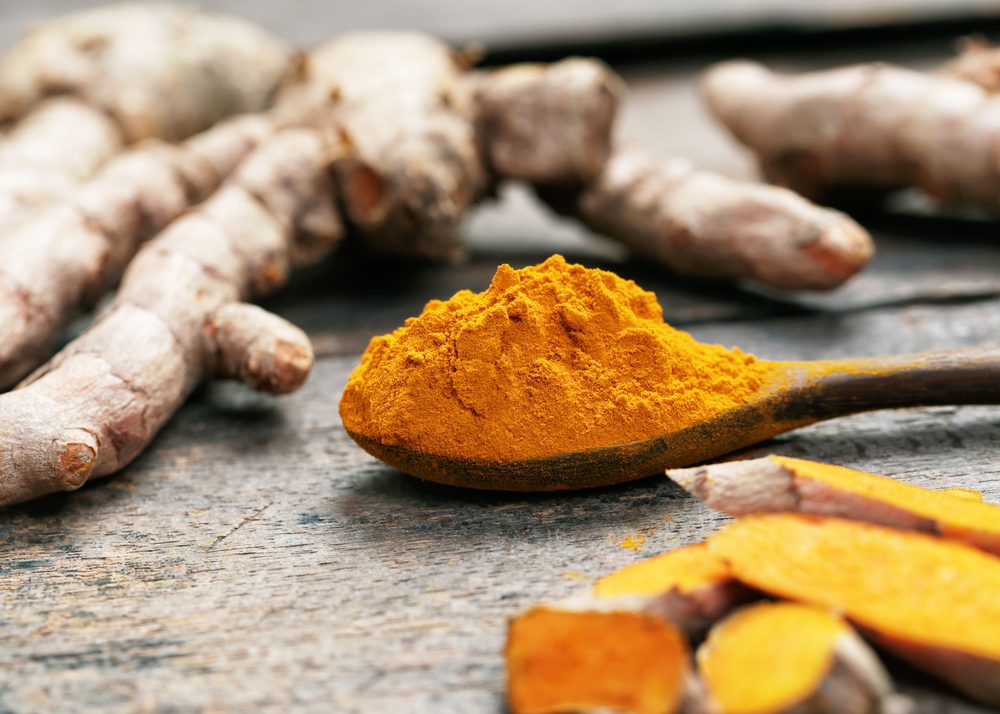 Turmeric powder and turmeric on wooden spoon.